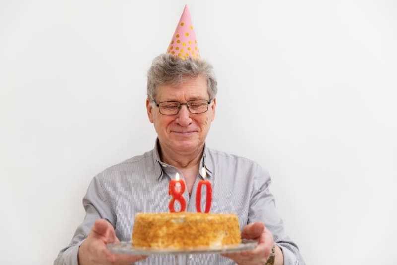80 모양의 촛불이 꽂힌 케이크를 들고 있는 중년 남성